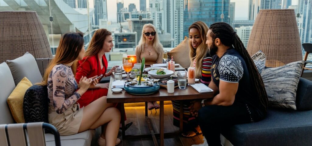 Image showing a group of friends around a dinner table with Dubai buildings in the background